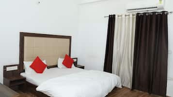 A hotel room with a bed, nightstands, a wooden floor, and an air conditioning unit.