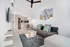 A modern living room with a glass coffee table, grey sofa, and artwork on the wall.