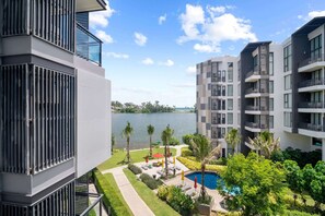 A modern apartment complex with balconies, a swimming pool, and a view of a lake.