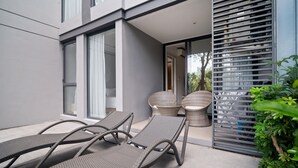 A modern outdoor seating area with wicker lounge chairs and a table, adjacent to a building with large windows and a sliding glass door. - Cassia Residences, One Bedroom 1103 A1 Ground Floor (Choeng Thale)