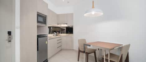 Una cocina moderna con electrodomésticos integrados, una zona de comedor con una mesa y sillas de madera, y una lámpara colgante.
