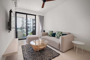 A modern living room with a sofa, a glass coffee table, a small side table, and a large window with curtains.