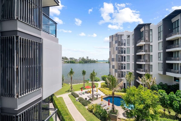 A modern apartment complex with balconies, a swimming pool, and a view of a lake.