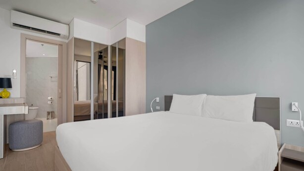 Een moderne hotelkamer met een groot bed, een nachtkastje, een klein krukje, een spiegel en een inloopkast.