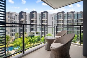 Un balcon doté de meubles en osier, offrant une vue sur un immeuble d’appartements moderne et une piscine.