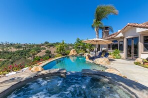 Une piscine avec un jacuzzi, des chaises longues et une vue sur le paysage environnant.