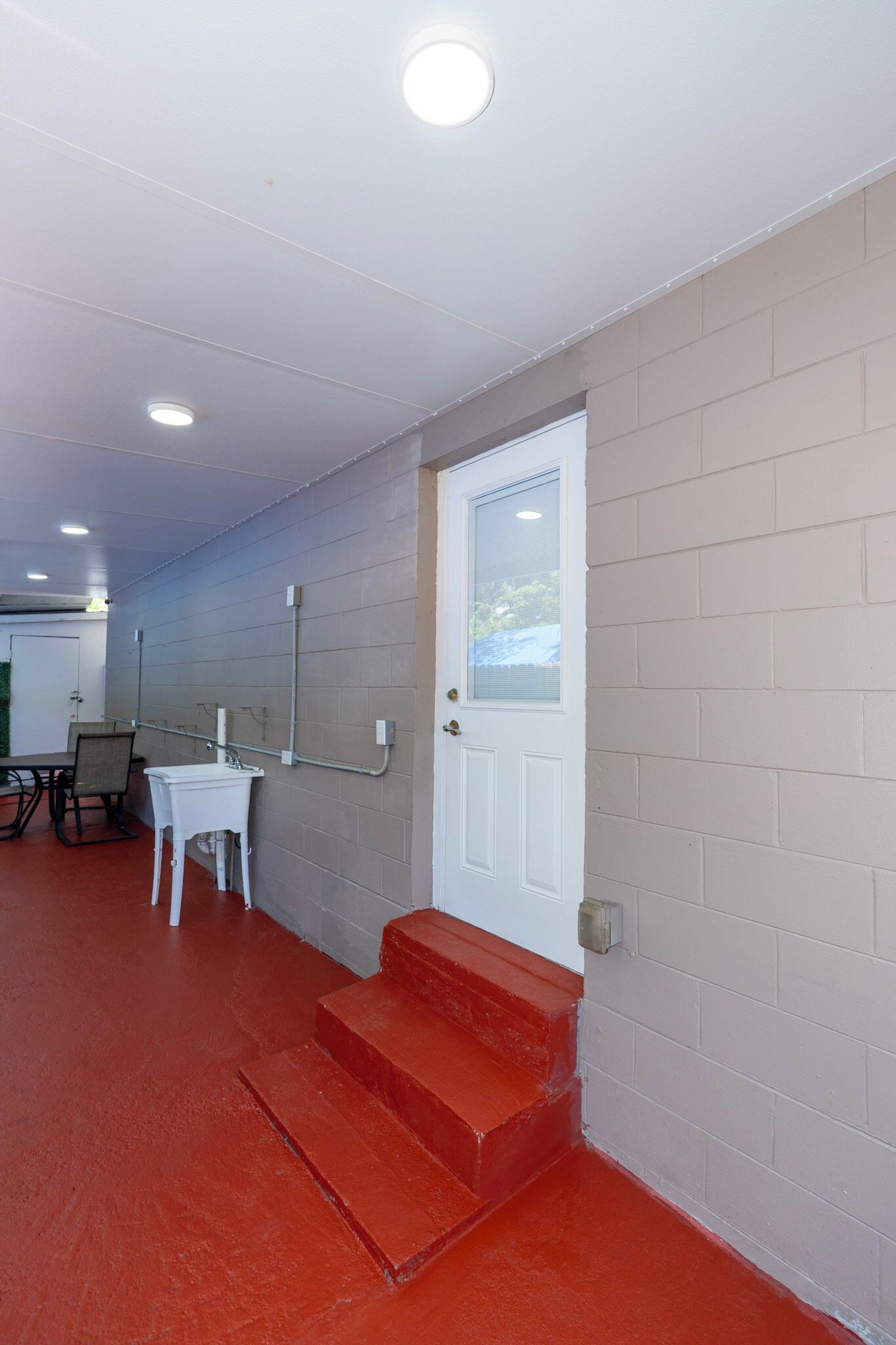 A hallway with a red carpet, a white door, a small table with a chair, and a window.