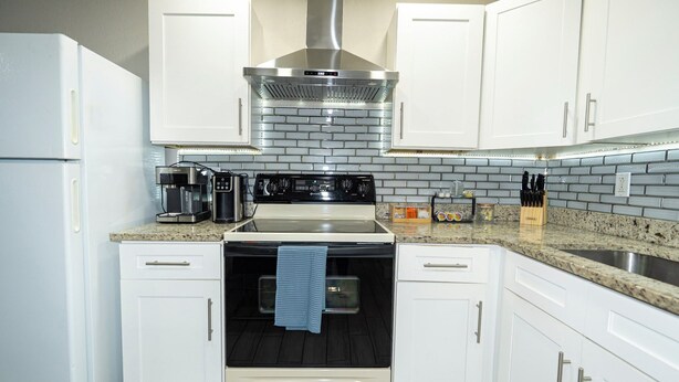 A kitchen with white cabinets, a stainless steel range hood, a built-in oven, a granite countertop, and a sink. - Spacious Home in CentralTampa near all attractions (Tampa)
