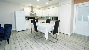 A modern kitchen with white cabinets, a white refrigerator, a dining table with chairs, and a microwave. - Spacious Home in CentralTampa near all attractions (Tampa)