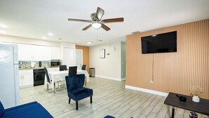 A modern living room with a ceiling fan, a flat-screen TV mounted on the wall, and a dining area with a table and chairs. - Spacious Home in CentralTampa near all attractions (Tampa)