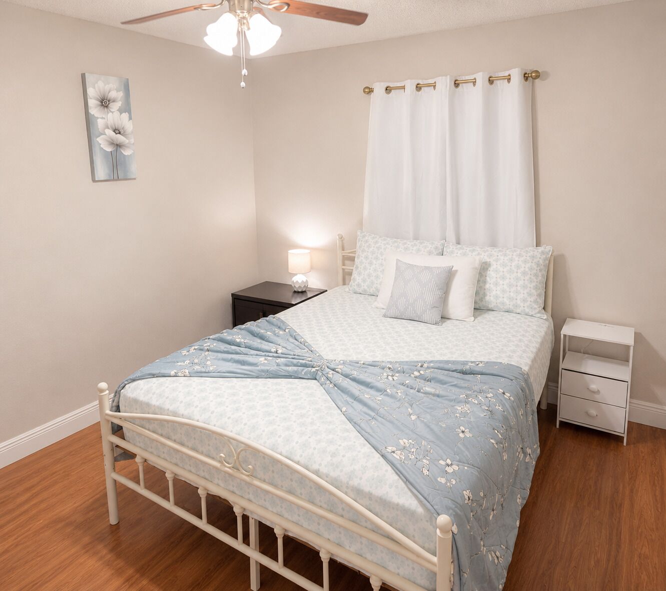 A bedroom with a bed, nightstands, a ceiling fan, a wall-mounted lamp, and a painting.
