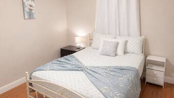 A bedroom with a bed, nightstands, a ceiling fan, a wall-mounted lamp, and a painting.
