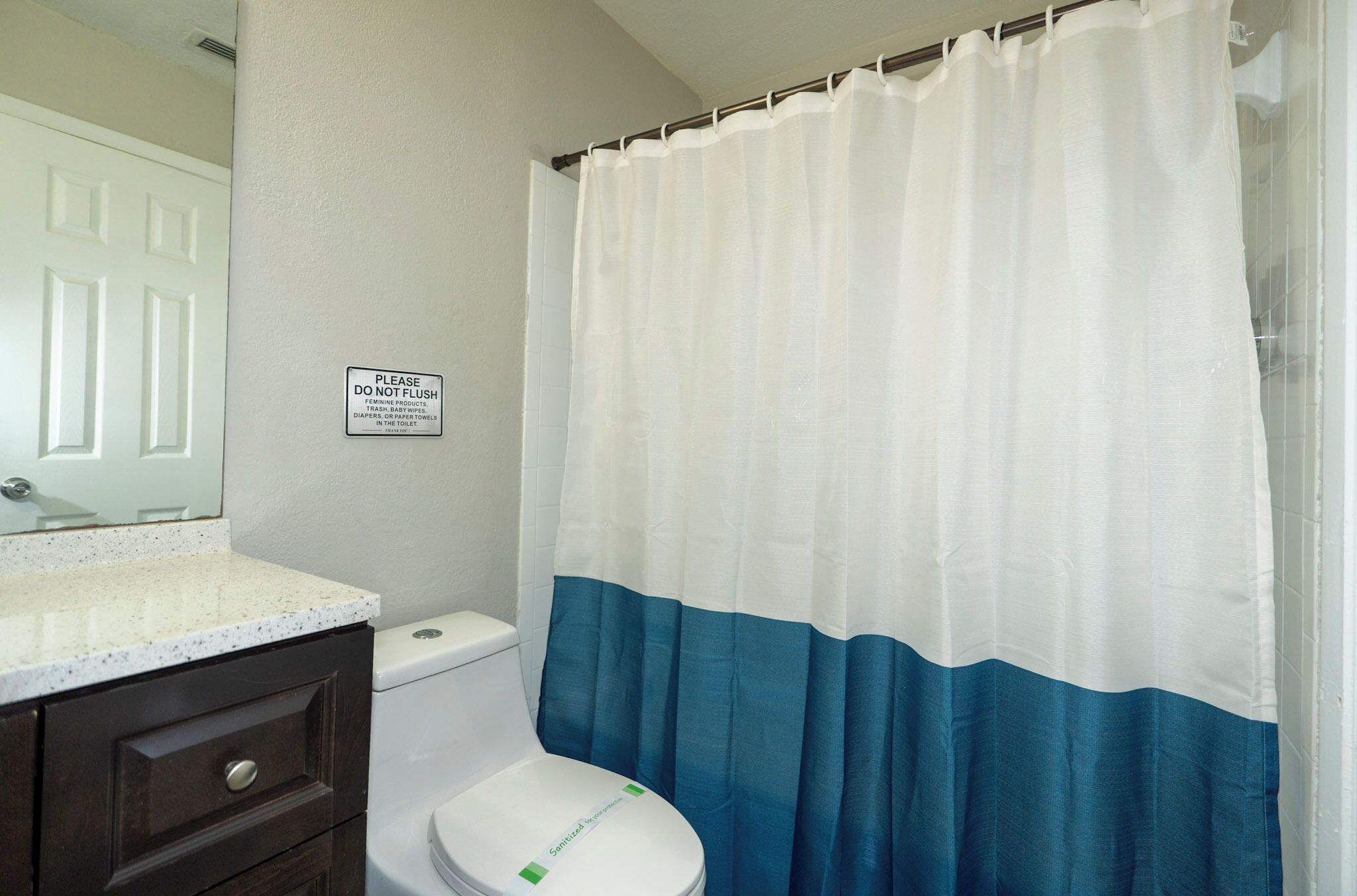 Un baño con inodoro, lavamanos con encimera y cortina de ducha.
