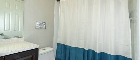 Un baño con inodoro, lavamanos con encimera y cortina de ducha.