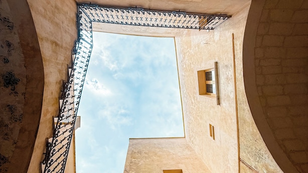 A narrow alleyway with a view of the sky through a small window, surrounded by old buildings with a rustic appearance.