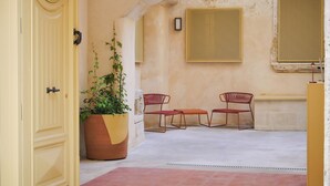 A courtyard with a yellow door, a large potted plant, two red chairs, and a small table.