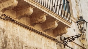 A building facade with a balcony featuring a black wrought-iron railing and a lantern-style light fixture.