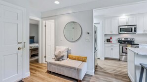 A modern apartment with a kitchenette, a round mirror, a bench with a cushion, and a door leading to a bedroom. - Condo Steps from Lake Pinneo, Fairway Village (Hartford)