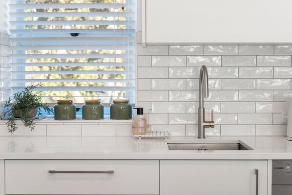A modern kitchen with white cabinetry, a stainless steel sink, and a window with blinds.