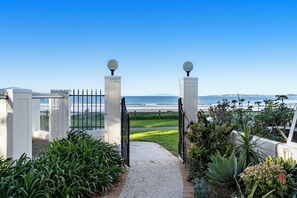 A gated entrance with a gravel path leading to a grassy area and a view of the ocean.