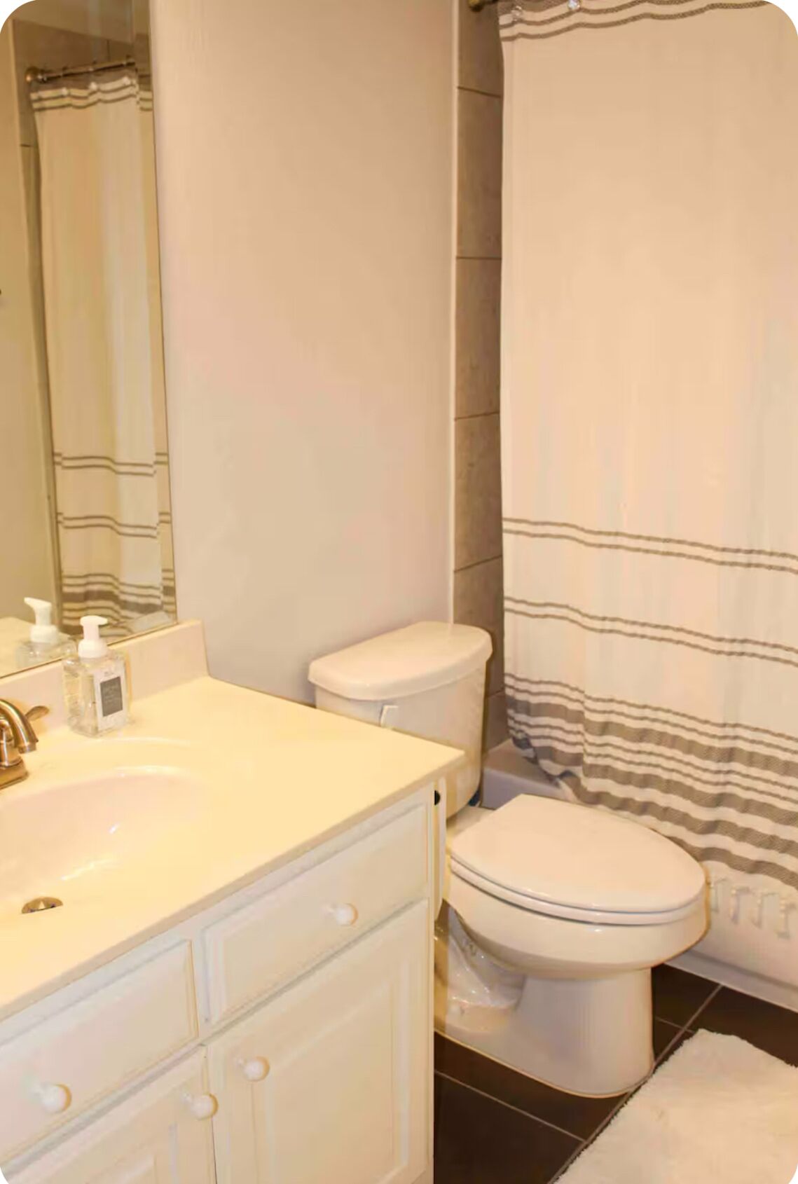 Un baño con un lavabo blanco, un inodoro y una cortina de ducha a rayas.