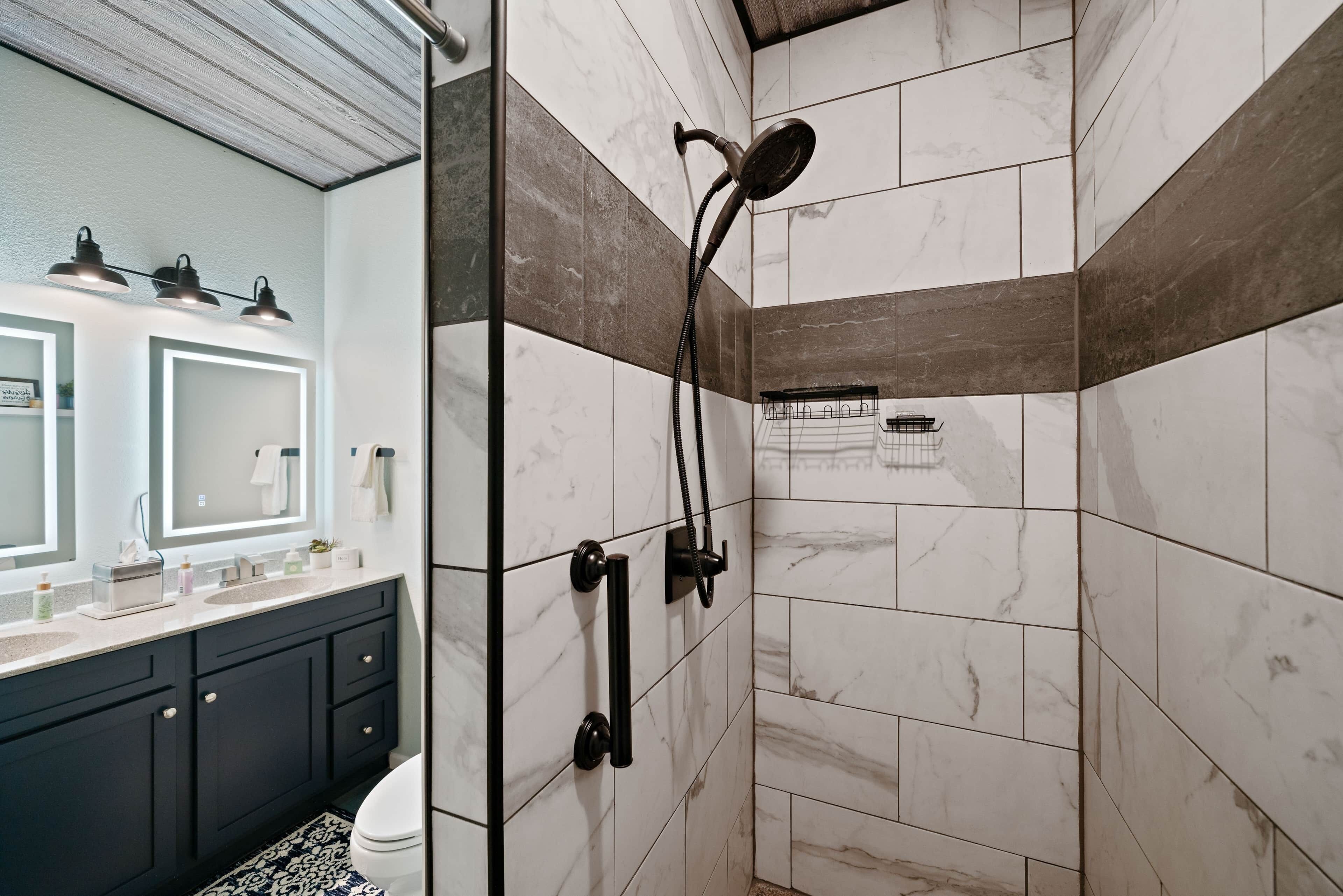 A modern bathroom with a walk-in shower, dark cabinets, a marble-tiled shower area, and a vanity with a mirror and countertop.