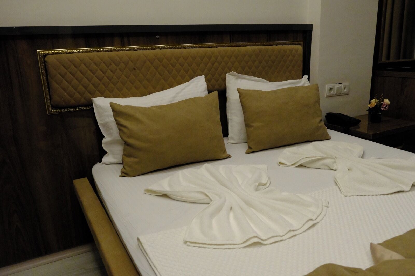Una cama bien hecha con un cabecero acolchado, dos almohadas marrones y toallas blancas.