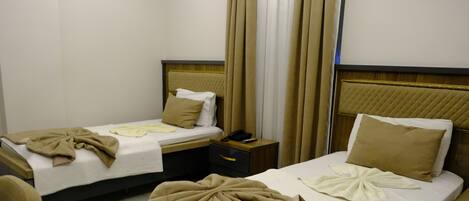 A hotel room with two beds, each with a beige blanket and pillow, a bedside table with a phone, and a nightstand with a lamp.