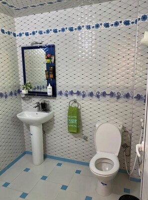 Et badeværelse med hvid vask, spejl, toilet og brusebad.
