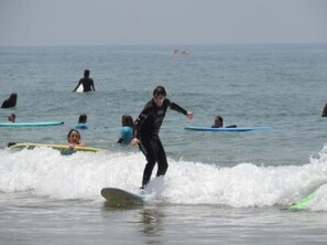 En person surfer på en bølge i havet, mens andre surfere ses i baggrunden.