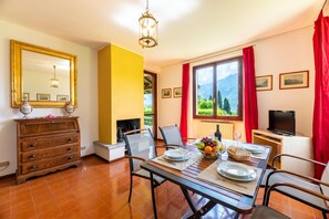 A dining area with a table set for two, a television, and a view of mountains through a window.