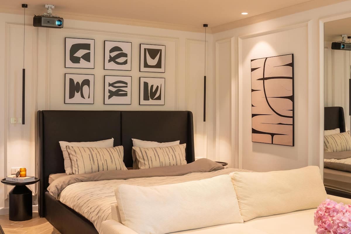 Une chambre moderne avec un grand lit, une table de chevet, une commode, un projecteur fixé au mur et des œuvres d’art abstraites accrochées au mur.