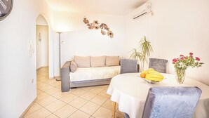 A living room with a sofa, a dining table with a vase of flowers, and a clock on the wall. - C apt w Terrace & sea View, 4 min Walk to Beach (Podstrana)