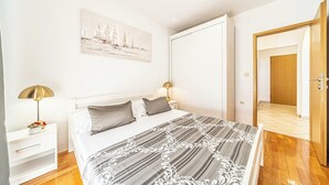 A bedroom with a bed, bedside tables, a lamp, a painting, and a door leading to another room. - C apt w Terrace & sea View, 4 min Walk to Beach (Podstrana)