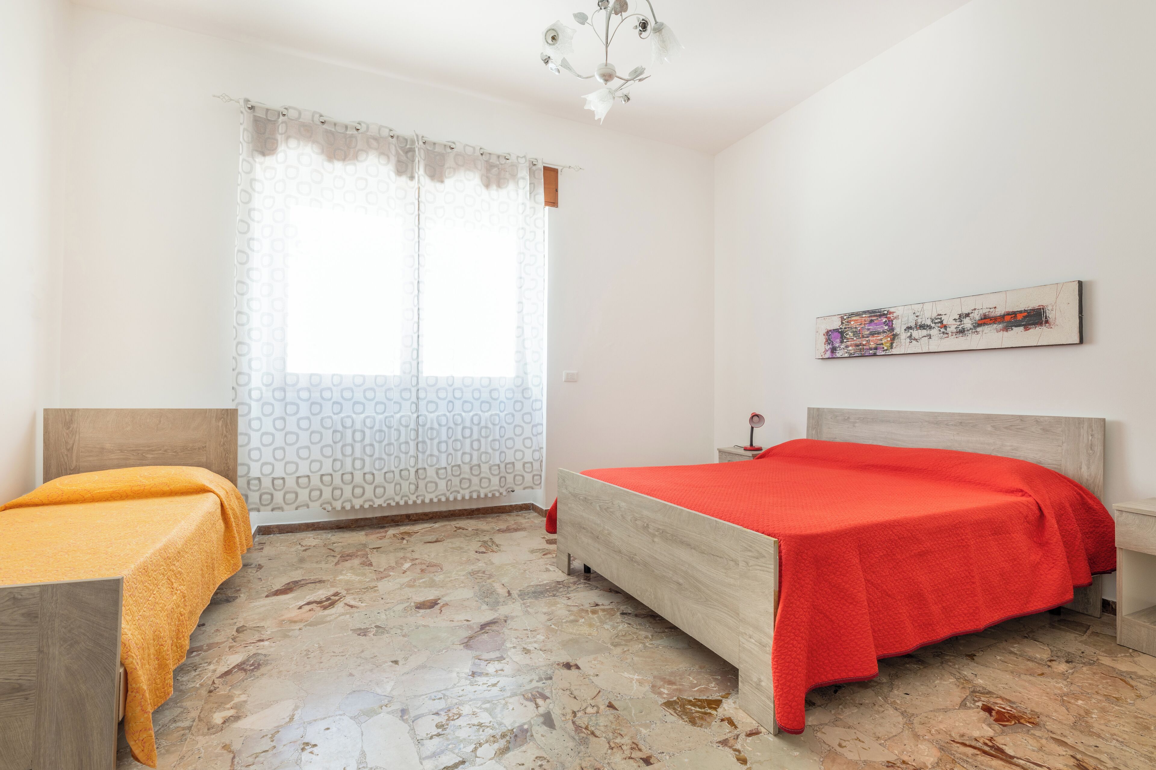 A bedroom with a bed, a nightstand, a window with curtains, and a painting on the wall.