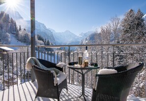 En balkon med fletstole og et lille bord, med udsigt over et sneklædt bjerglandskab.