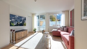 Een ruime woonkamer met een groot raam, een rode bank, een wit tapijt en een kast.