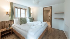 Une chambre d’hôtel moderne avec un grand lit, une tête de lit en bois et une vue sur le couloir.