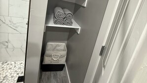 Un pasillo estrecho con una puerta blanca, suelo de baldosas de mármol y una pequeña planta en un estante.
