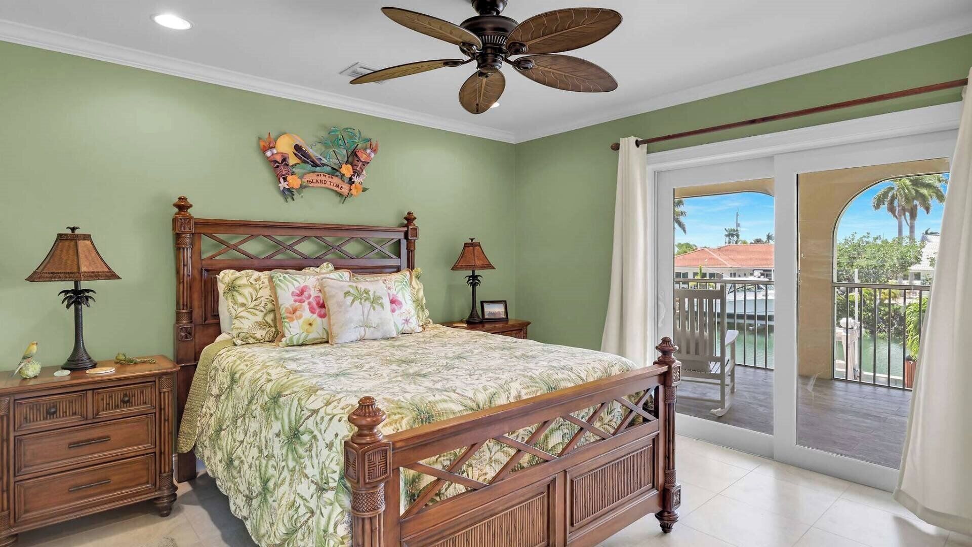 A bedroom with a bed, nightstands, a ceiling fan, and a view of the outdoors.