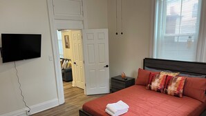 A bedroom with a bed, a nightstand, a TV, and a door leading to another room. - Outstanding spacious 2-bedroom Apt in downtown Cincinnati with many amenities (Cincinnati)