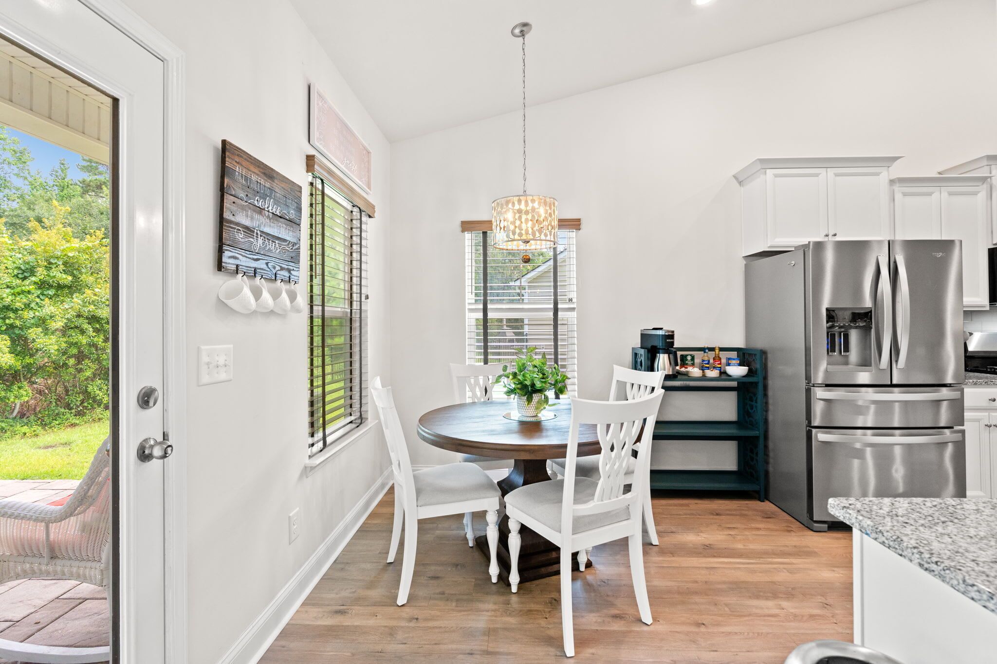 A modern kitchen with white cabinetry, a stainless steel refrigerator, and a dining area with a wooden table and white chairs.