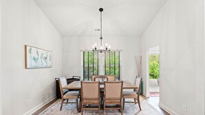 A dining room with a chandelier, a table with chairs, a rug, and a window with greenery outside. - 3BR Legends Golf Home | Bunk Room + Backyard (Myrtle Beach)