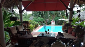 A poolside seating area with a table set for a meal, surrounded by lush greenery and a thatched roof structure. - Belle propriété de style Caraïbes, confortable chambre d'hôtes, piscine privée (Las Terrenas)