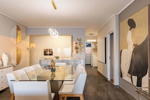 Un comedor moderno con una mesa de vidrio, sillas blancas y una lámpara central.