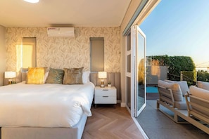 Un dormitorio con cama, mesitas de noche, lámpara, ventana y balcón con piscina.