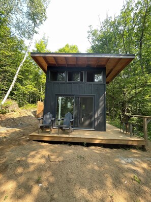 A modern cabin with a deck, two chairs, and a large window.