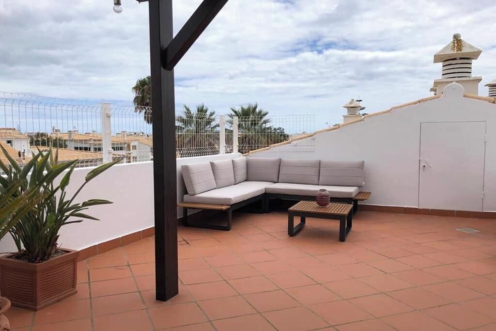 Una terraza en la azotea con un sofá blanco, una mesita y una planta en maceta.
