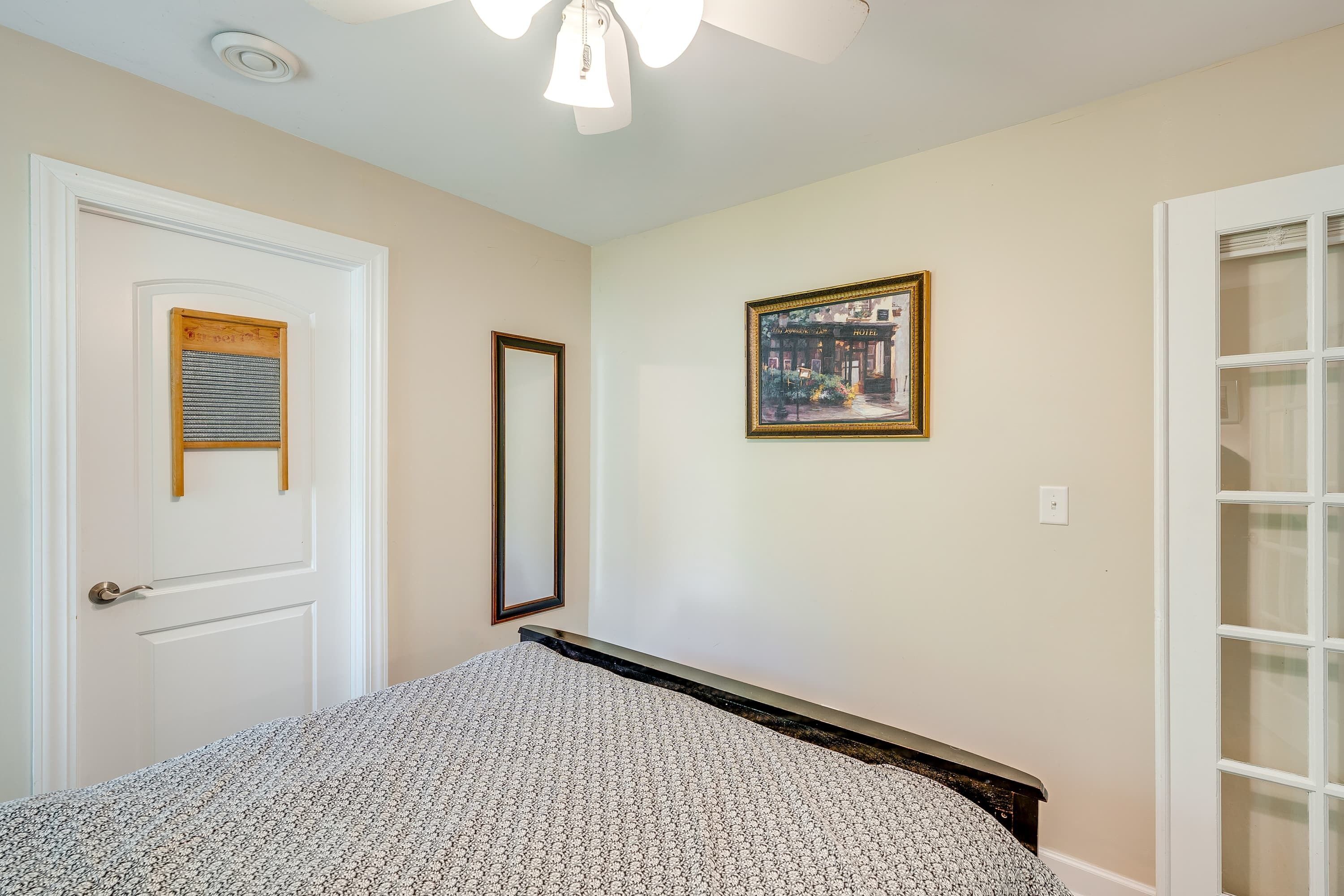 A bedroom with a bed, a door with a window, a framed picture on the wall, and a ceiling fan.