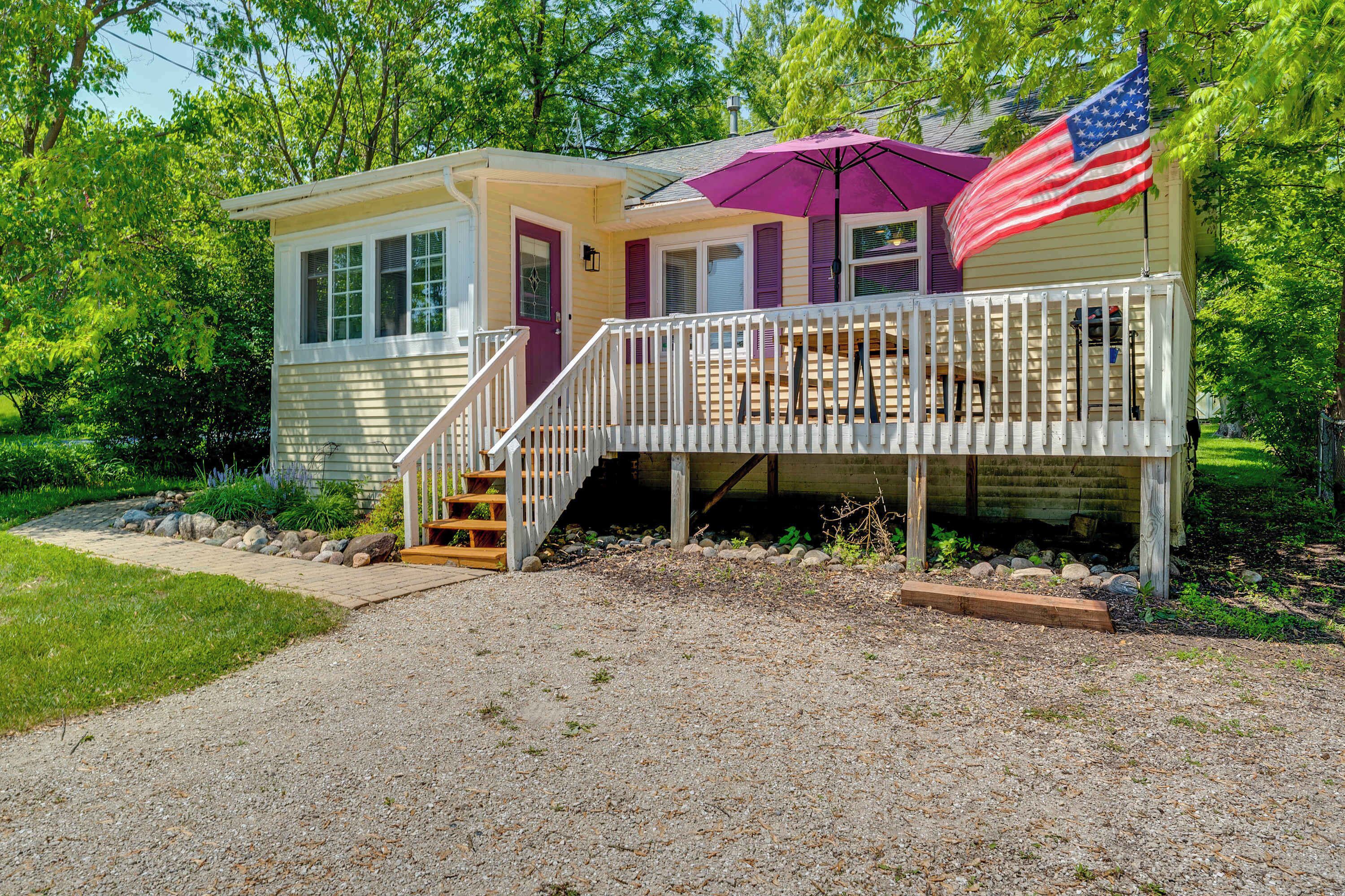 A small, single-story house with a front porch, a staircase leading to the entrance, and an American flag on the right side.